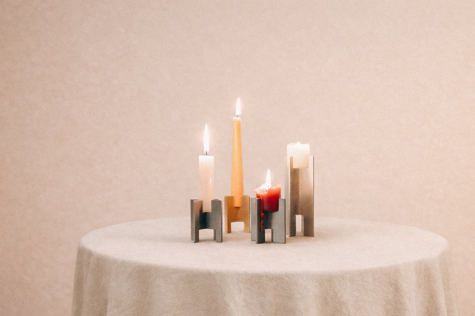 Minimalist Lyssier candleholders in brushed and polished metal, holding lit taper and pillar candles in different sizes, arranged on a neutral background showcasing material contrast, precision, and sculptural form.