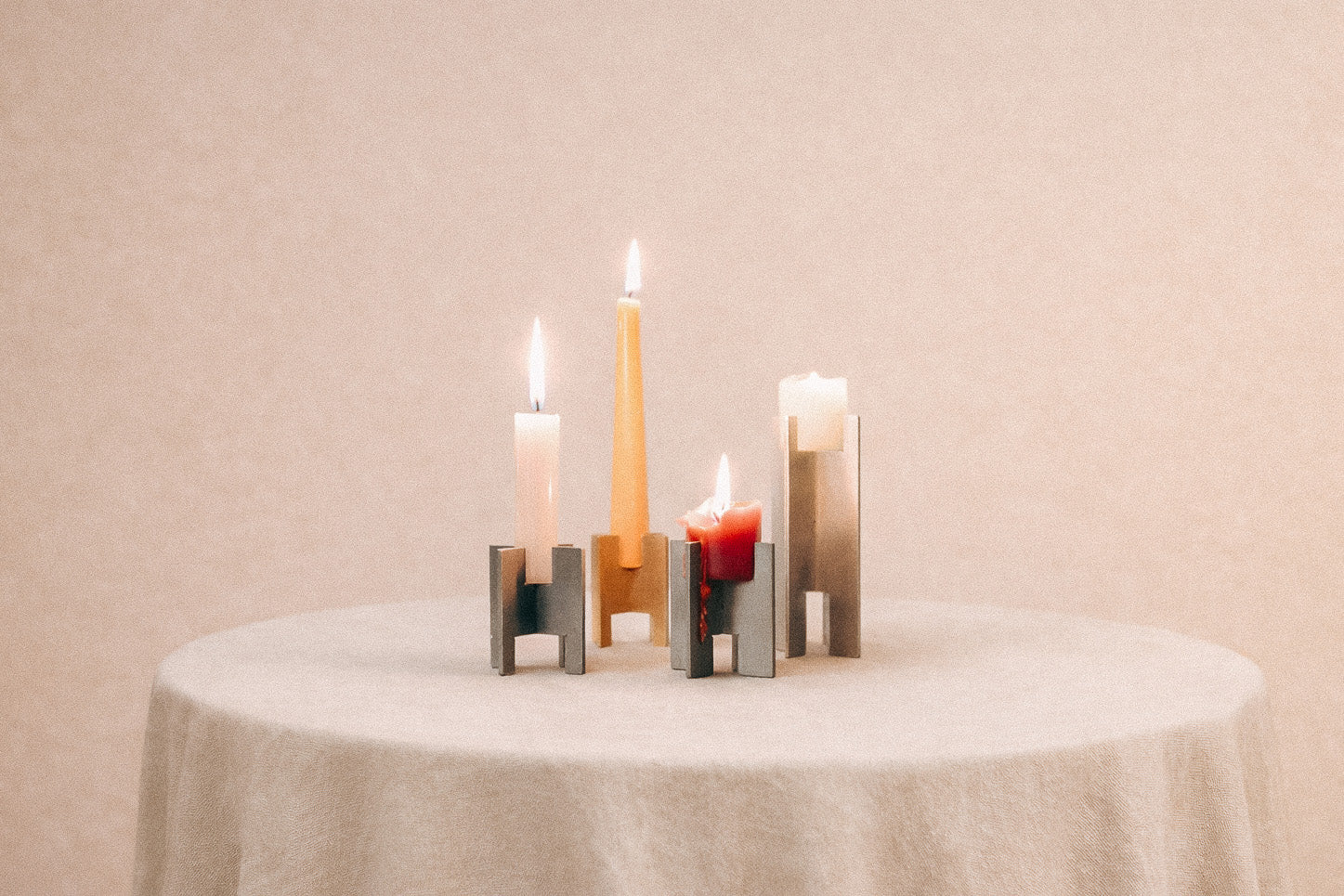 Minimalist Lyssier candleholders in brushed and polished metal, holding lit taper and pillar candles in different sizes, arranged on a neutral background showcasing material contrast, precision, and sculptural form.