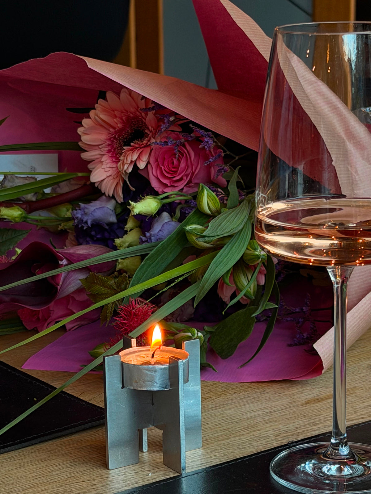 Lyssier H64 stainless steel candleholder with a lit tealight beside a glass of wine and fresh flowers on a dinner table.