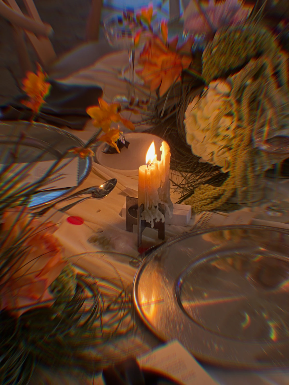 Lyssier H64 candleholder from stainless steel with a lit taper candle on a dinner table surrounded by flowers, glass bottles and tableware.