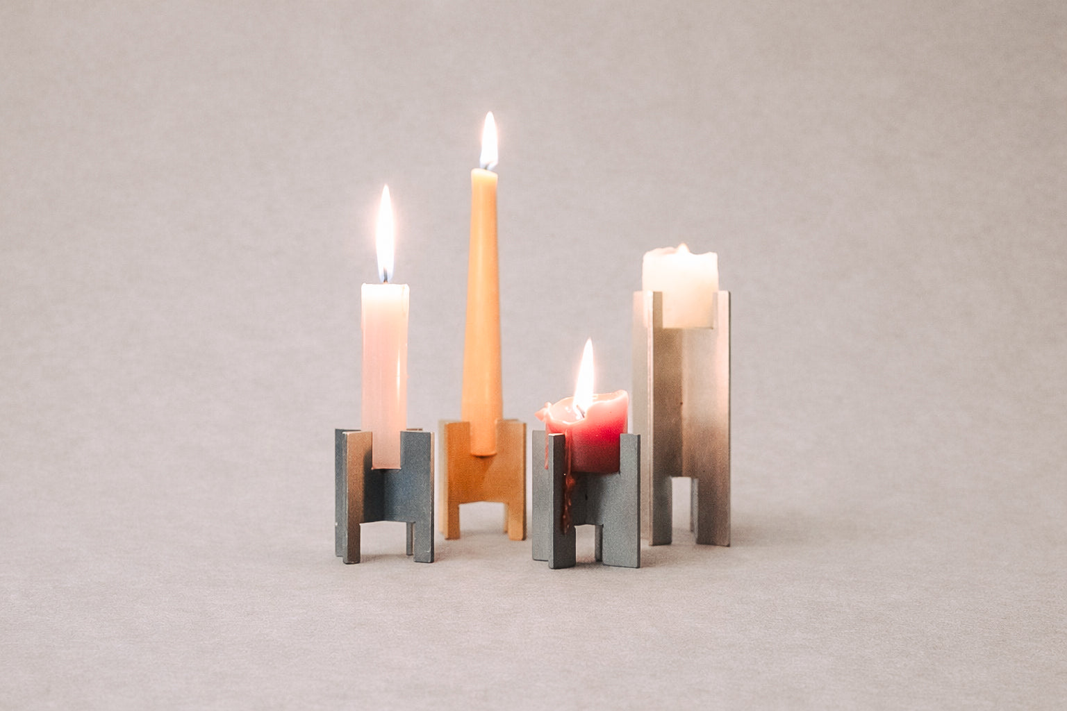 Minimalist Lyssier candleholders in brushed and polished metal, holding lit taper and pillar candles in different sizes, arranged on a neutral background showcasing material contrast, precision, and sculptural form.
