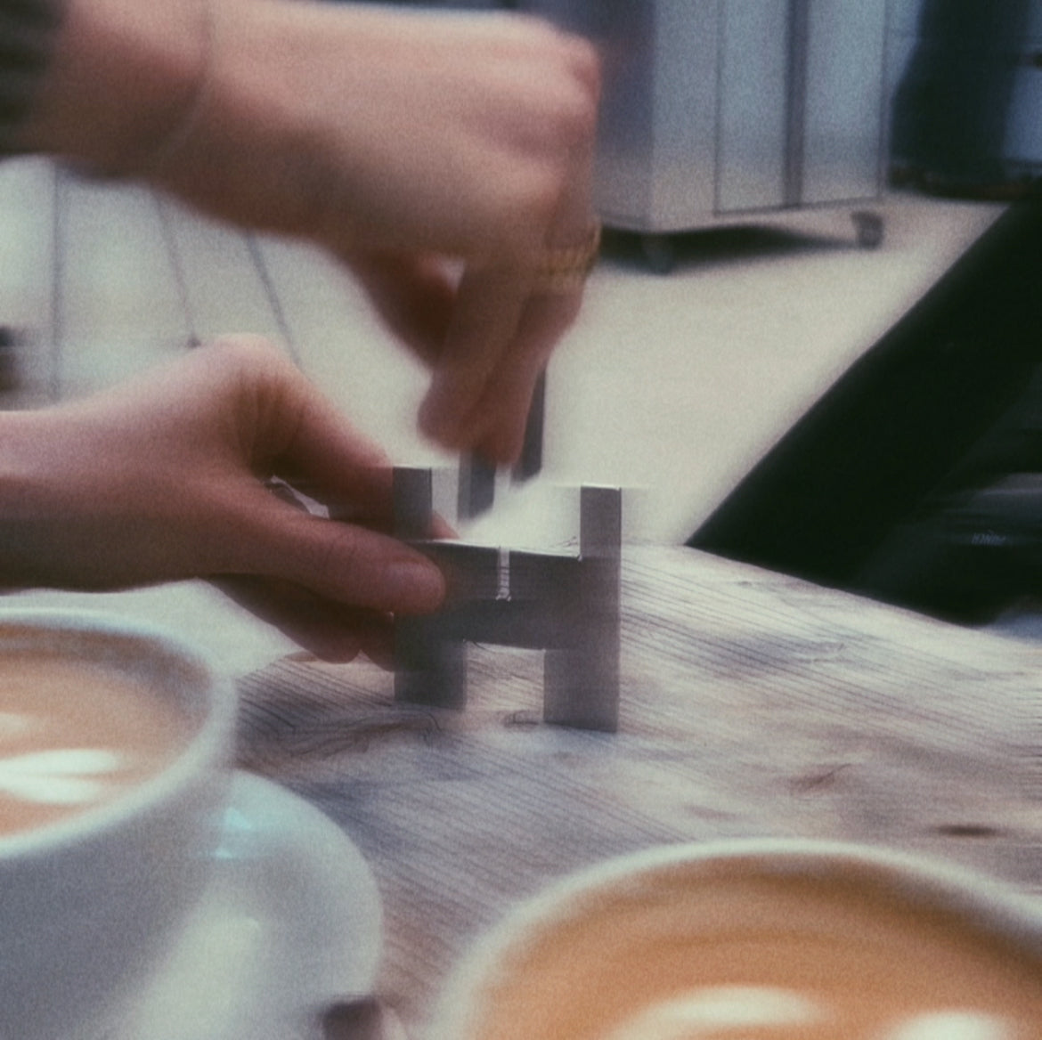 Lyssier H64 metal candleholder assembled by two hands on a wooden table, next to two cappuccinos.